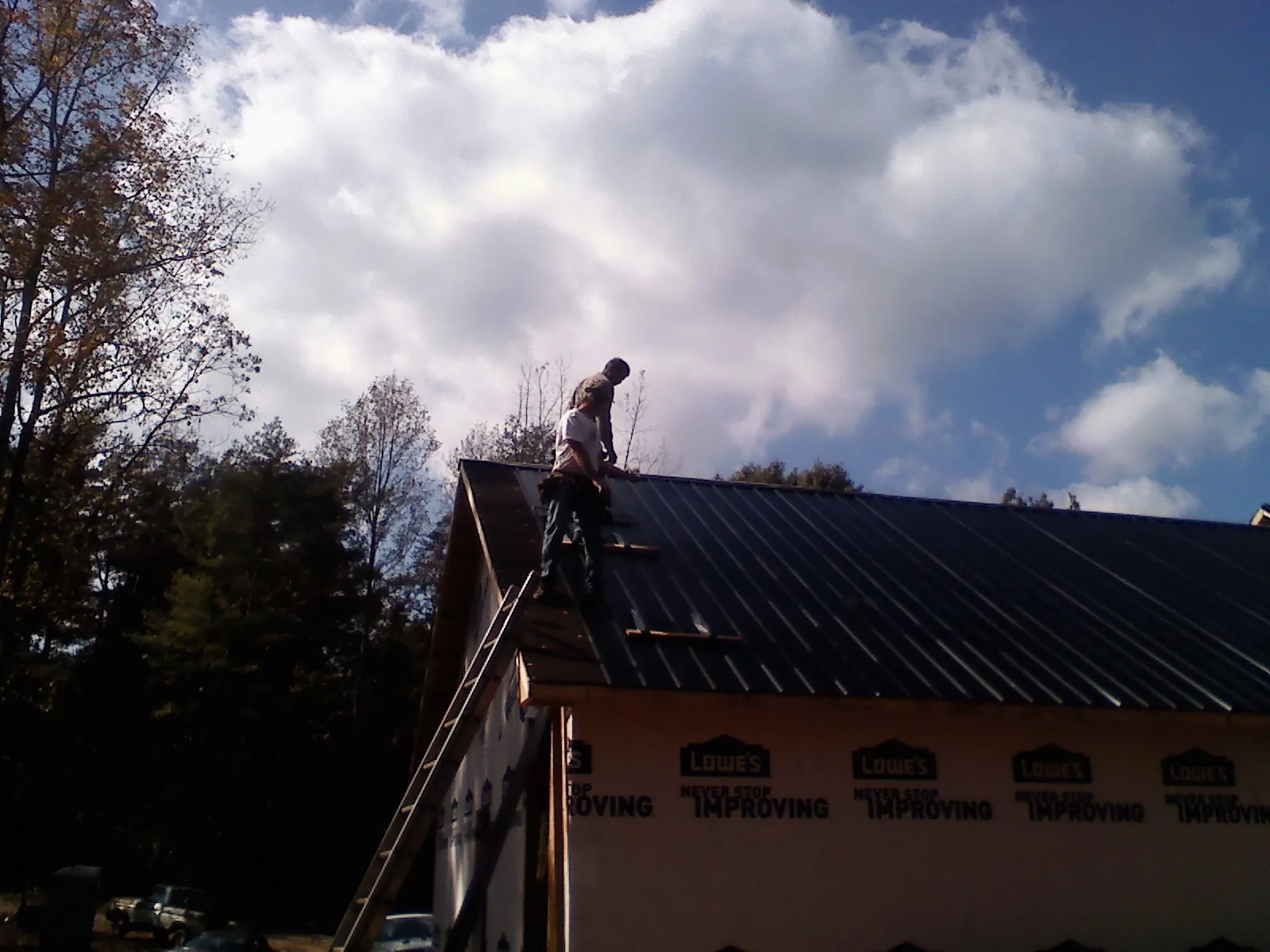 Roofer fastening dark metal panels high against a cloudy sky, from a Roof Inspection job in Metamora