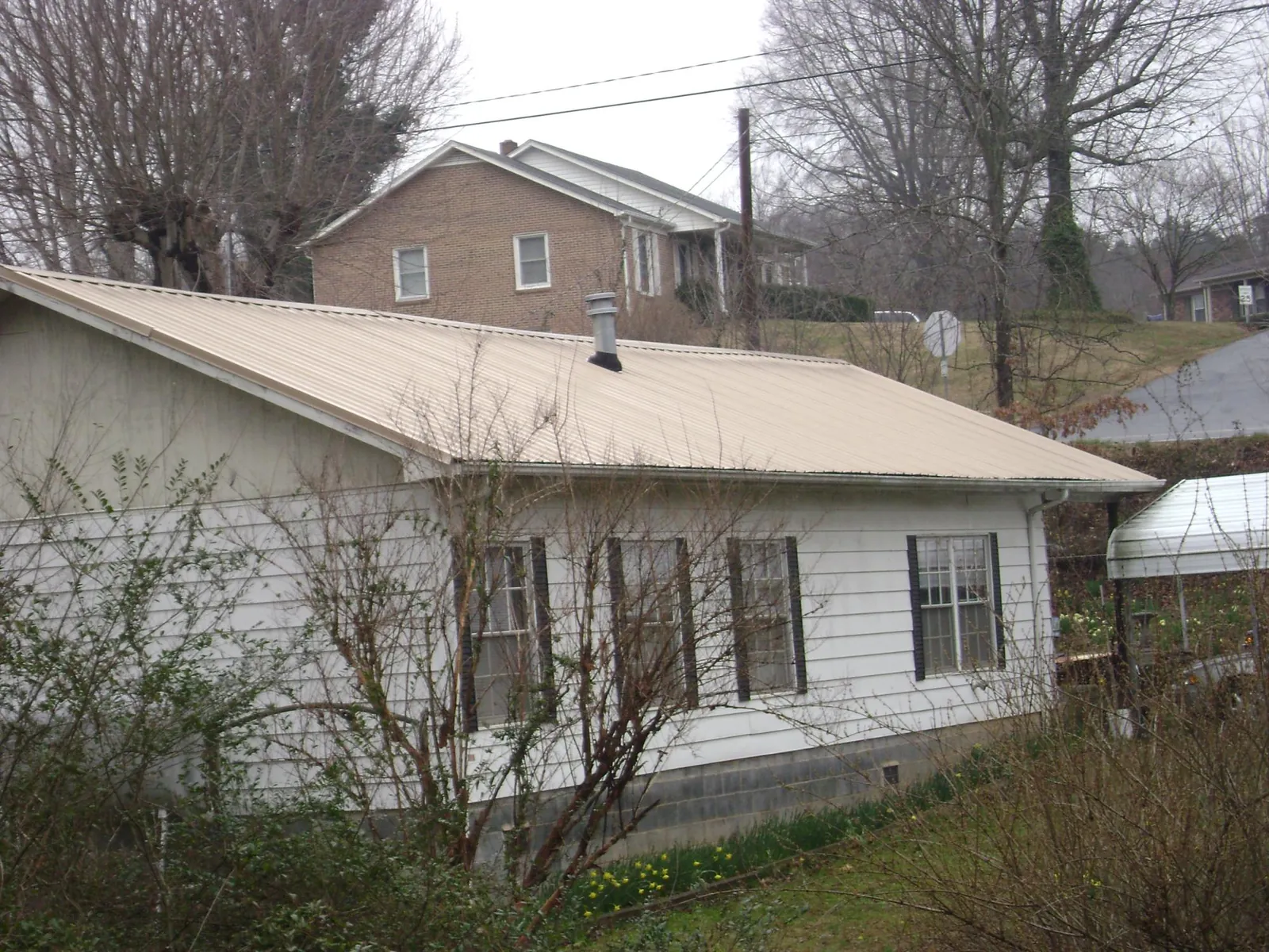 Tan metal roof on a white sided house set into a hillside — Commercial Roofing by Roofing Brothers in Metamora