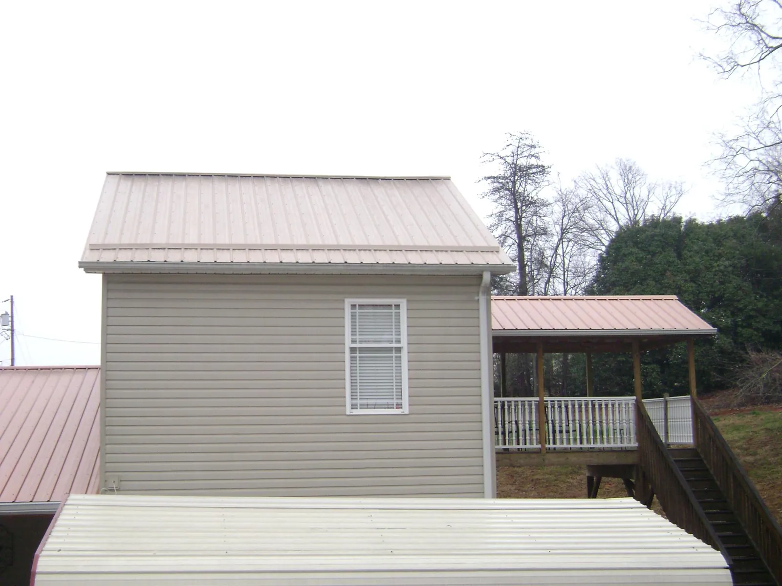 Tan metal roofs on a two story addition and attached porch, from a Roof Replacement job in Metamora